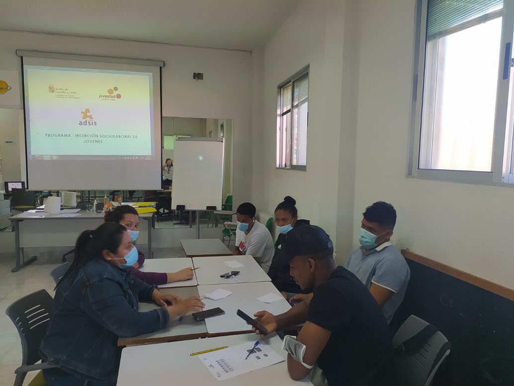 Cinco jóvenes alrededor de una mesa en una aula, con un proyector en el fondo