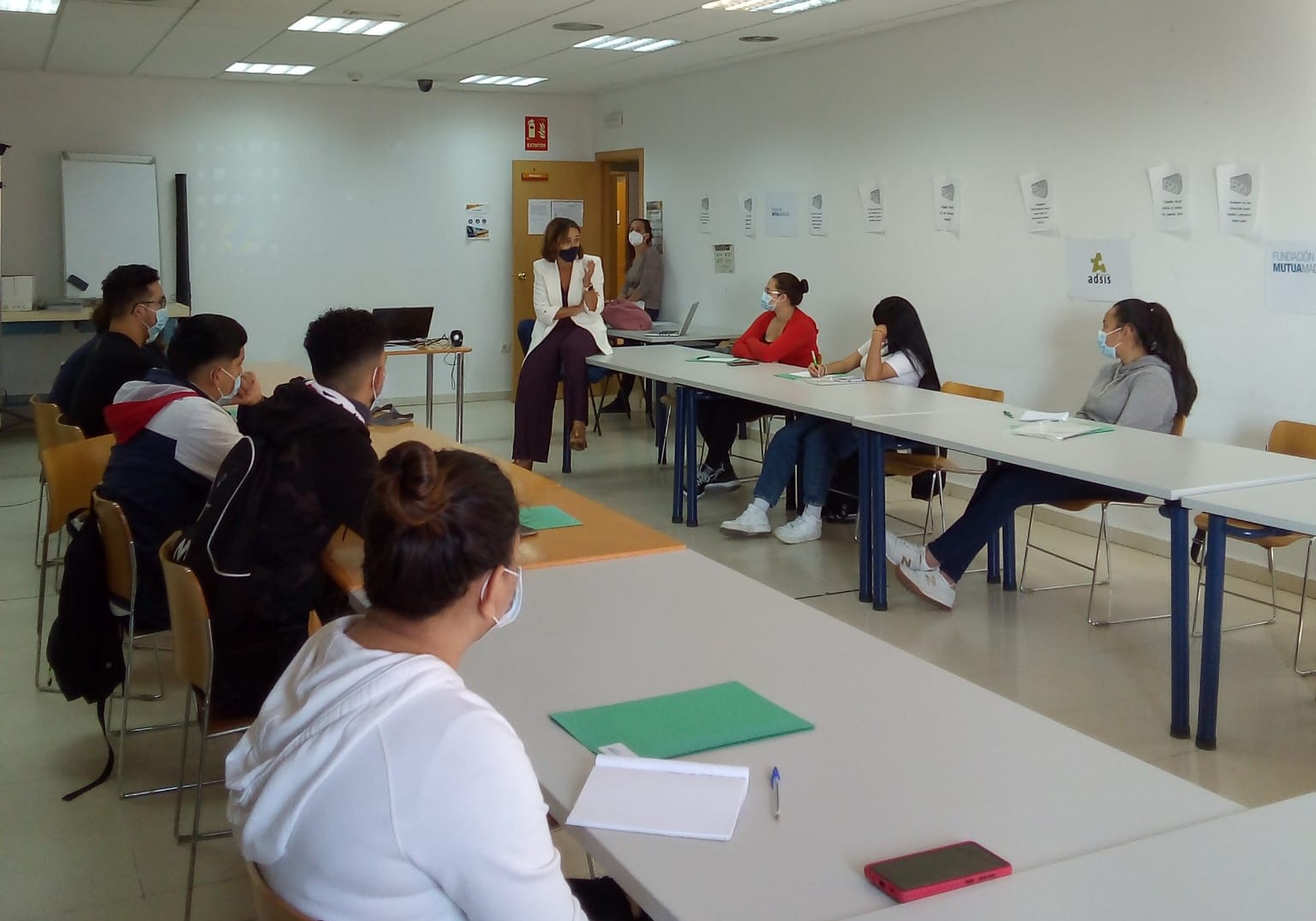 Un grupo de jóvenes sentados en una aula escuchando a una mujer que les explica algo