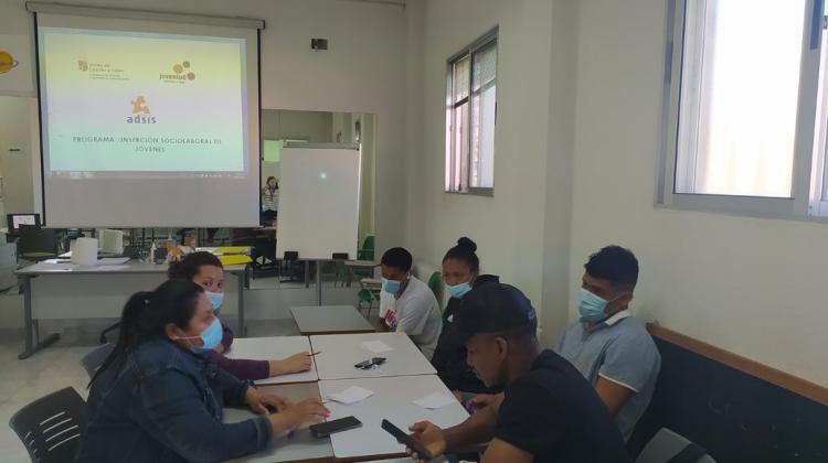 Cinco jóvenes alrededor de una mesa en una aula, con un proyector en el fondo